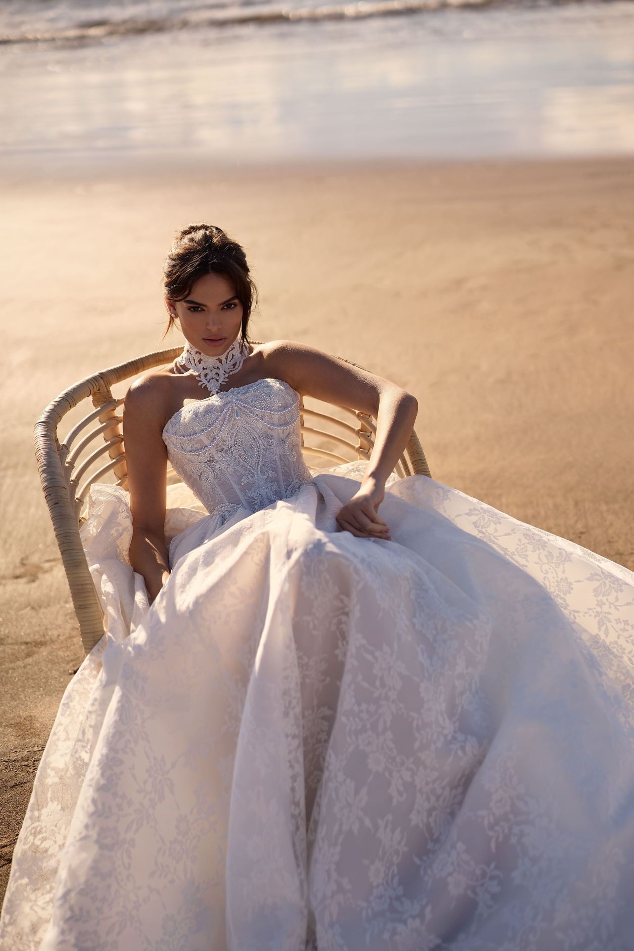 Milla Nova lace wedding gown worn by a model seated on a beach